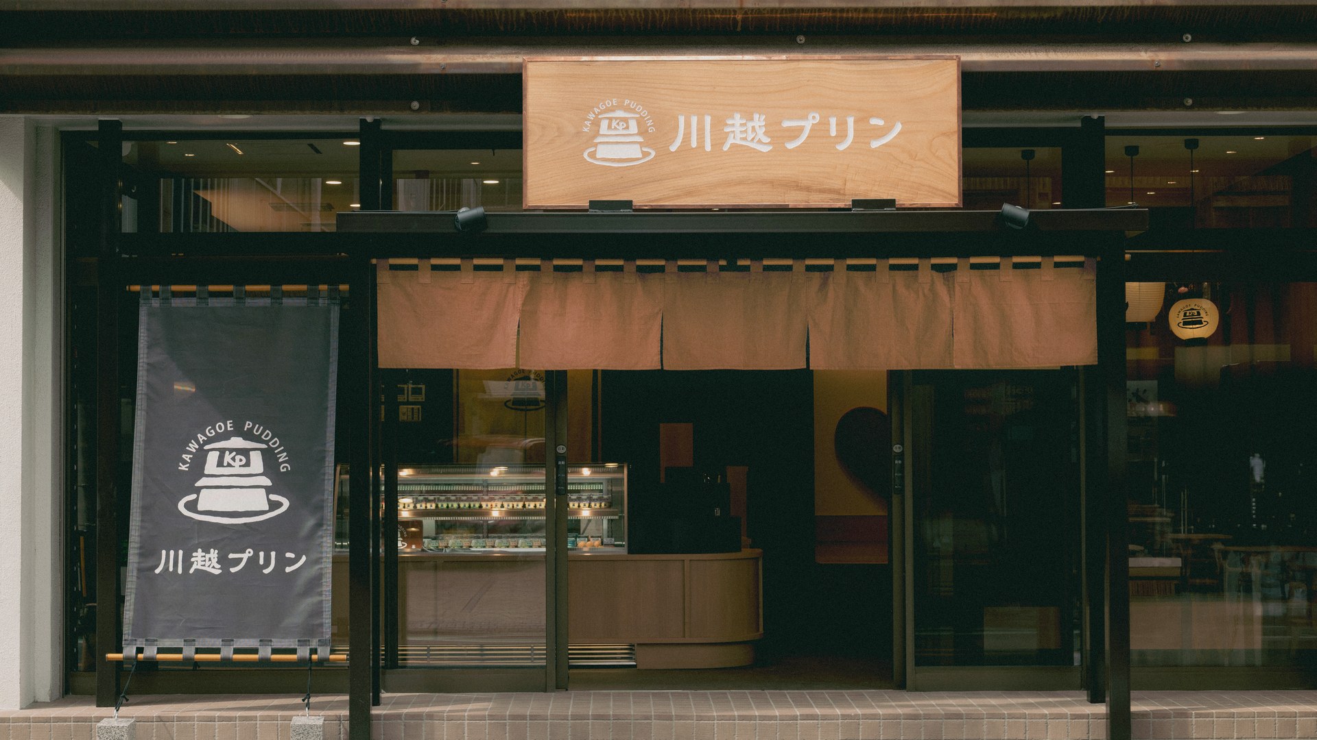 リニューアル後の川越プリン2号店の外観。木の看板とのれん、店頭ののぼりに新しいロゴが展開されている