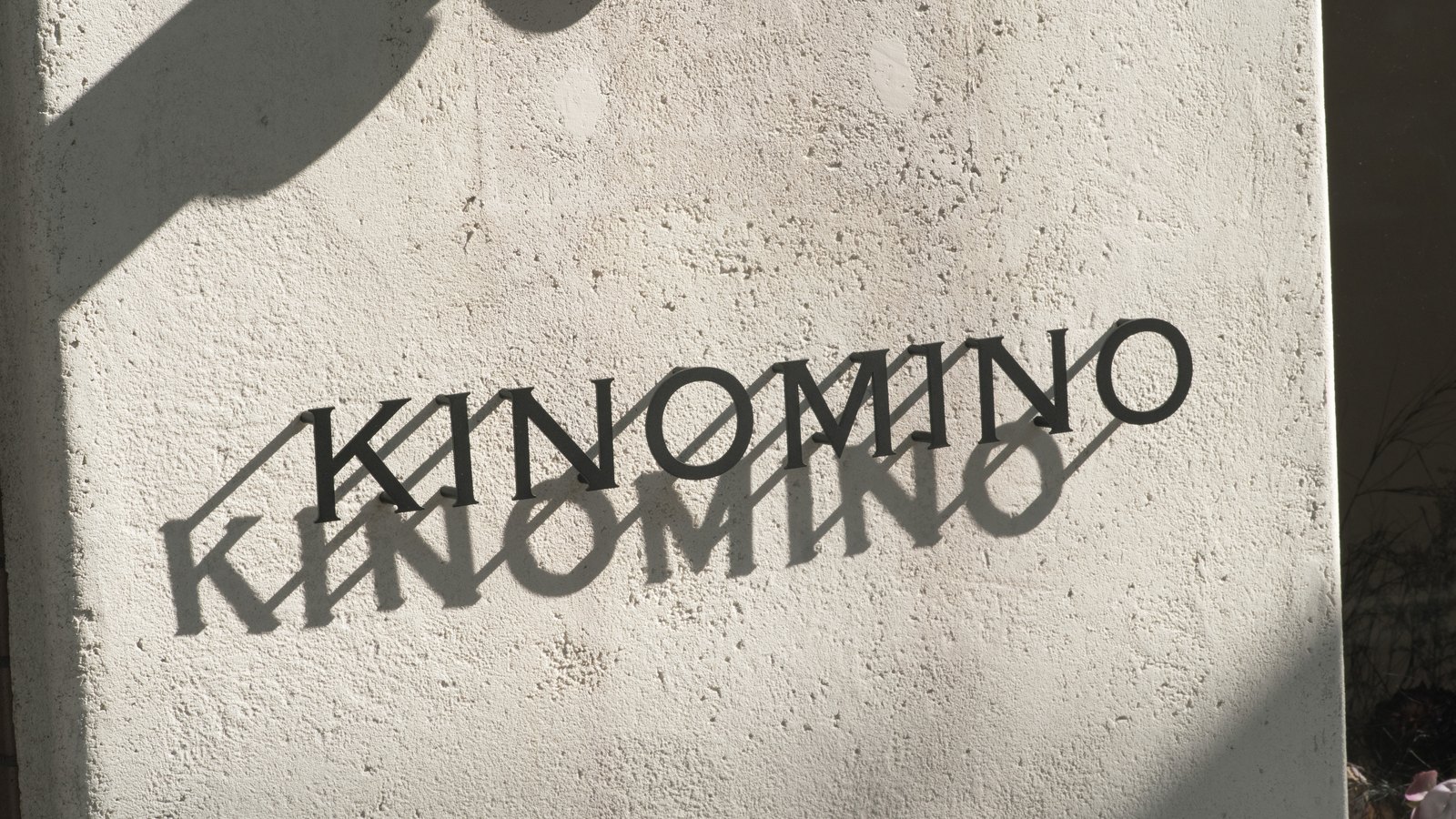 KINOMINOの店舗サイン。白い塗り壁に切り文字のロゴが取り付けられ、影が落ちている